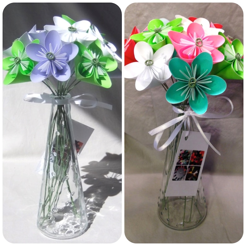 Puede incluir: Un jarr&oacute;n de cristal transparente contiene un ramo de flores de origami en varios colores, incluyendo morado, blanco, verde, rosa y rojo. Las flores est&aacute;n atadas con una cinta blanca. Una peque&ntilde;a etiqueta cuelga del jarr&oacute;n.