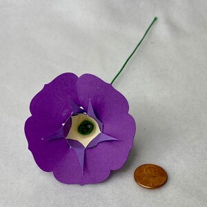 Puede incluir: Una flor de papel morada con un centro blanco y un tallo verde. La flor es aproximadamente del tama&ntilde;o de una moneda de un c&eacute;ntimo de euro.