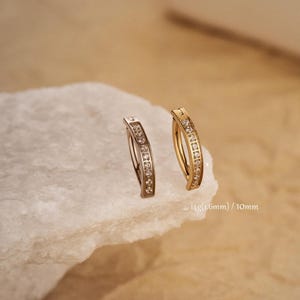 May include: Two gold and silver hoop earrings with a row of clear cubic zirconia stones. The earrings are 6mm and 10mm in diameter.