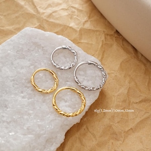 Può includere: Quattro orecchini a cerchio, due dorati e due argentati, con un design a corda intrecciata. Gli orecchini sono esposti su una superficie bianca strutturata su sfondo marrone. Testo: 16g(1,2mm)/10mm,12mm.