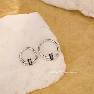 May include: Two silver-colored hoop earrings with a black rectangular stone in the center. The earrings have a double-band design and are displayed on a white, textured surface. The text on the image reads: 16g(1.2mm) / 8mm,10mm.