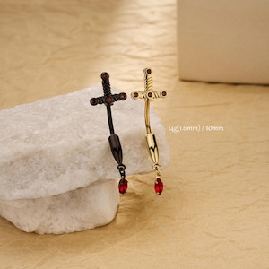 May include: Two belly button rings in the shape of swords. One is black with red accents, the other is gold with red accents. The text on the side reads "14g (1.6mm) / 10mm".