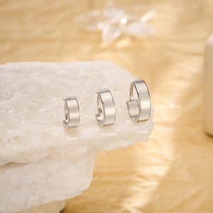 Könnte beinhalten: Drei silberfarbene Creolen in verschiedenen Größen werden gezeigt. Die Ohrringe haben einen Durchmesser von 8 mm, 10 mm und 12 mm. Die Ohrringe haben ein flaches, rechteckiges Design.