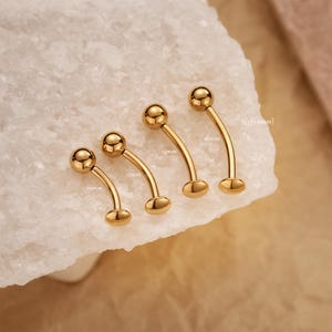 May include: Four gold-colored curved barbell piercings with ball ends and flat disc ends. The piercings are displayed on a white surface. Measurements are 10mm, 12mm, 14mm, and 16mm, with the 16mm piece also labeled as 14g (1.6mm).