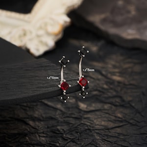 May include: Two curved barbell body jewelry pieces featuring square-cut stones. One piece is labeled 1.2*6mm with a black stone at the top and a red stone at the bottom. The other is labeled 1.2*8mm with a red stone at the top and a black stone at the bottom.