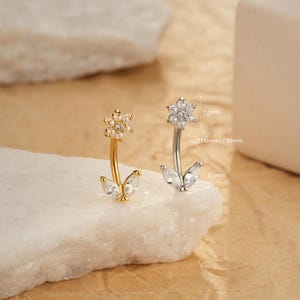 Puede incluir: Dos piercings curvos para cejas, uno dorado y otro plateado, cada uno con un diseño floral. La parte superior de cada anillo presenta una flor con pequeños acentos redondos. La parte inferior de cada anillo tiene dos acentos en forma de hoja. El anillo plateado mide 7,3 mm y 6,3 mm.