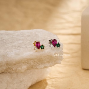 Peut inclure: Boucles d'oreilles à clous avec un design en grappe. Chaque boucle d'oreille comporte une pierre précieuse magenta en forme de goutte d'eau, une petite pierre verte et des pierres d'accent claires. Les boucles d'oreilles sont serties sur une base dorée et argentée.