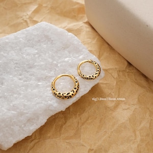 May include: Two gold-colored hoop earrings with a black leopard print design. The earrings are displayed on a white surface with a brown paper background. Text on the image reads: 16g(1.2mm)/8mm,10mm.