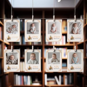 May include: A series of eight baby milestone photo prints, each featuring a different baby photo. The prints are held by clothespins on a string. Each print has text indicating the baby's age, from newborn to seven months.