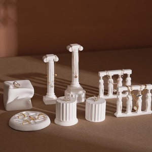 May include: White ceramic display stands in the shape of columns and a row of women. The stands are used to display jewelry, including necklaces, earrings, and rings.