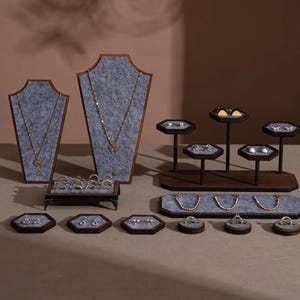Könnte beinhalten: Eine Präsentation von goldenem Schmuck, darunter Halsketten, Ringe und Ohrringe, auf verschiedenen Präsentationsständern aus Holz und grauem Filz. Der Hintergrund ist einfarbig und neutral.