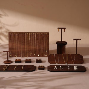 Könnte beinhalten: Schmuckpräsentation auf Holzständern und -tabletts. Die Ausstellung umfasst goldene Halsketten, Ohrringe und Ringe. Die Holzelemente sind dunkelbraun, und der Schmuck ist zur Präsentation angeordnet.