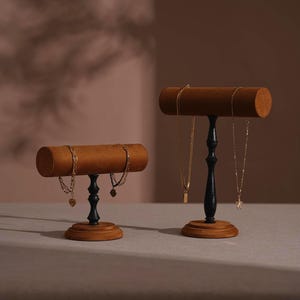 May include: Two wooden jewellery display stands. Each stand has a brown, cylindrical top and a black, ornate stem. The bases are round and made of wood. Gold necklaces and bracelets are displayed on the stands.