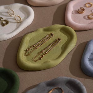 May include: A collection of small, decorative trays in various pastel colors, including white, pink, green, and blue. Each tray holds jewelry, such as earrings and bracelets. The bracelets are gold-toned with small, clear stones.