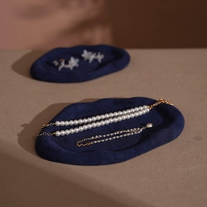 May include: Two navy blue felt jewelry trays. One tray holds a pearl necklace and a delicate pearl bracelet. The other tray holds a pair of floral earrings. The trays are on a neutral surface.