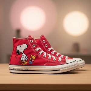 K&ouml;nnte beinhalten: Rote High-Top-Sneaker mit Snoopy- und Woodstock-Design. Die Schuhe haben wei&szlig;e Schn&uuml;rsenkel, eine wei&szlig;e Gummisohle und einen schwarzen Streifen. Der Text "Undercoverproduct" ist auf der wei&szlig;en Sohle aufgedruckt.