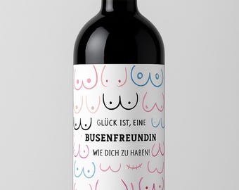 Op de afbeelding: Een zwarte wijnfles met een rode dop en een wit etiket. Het etiket toont een patroon van borsten in roze, blauw en zwart, met Duitse tekst. De tekst luidt "Glück ist, eine Busenfreundin wie dich zu haben!"
