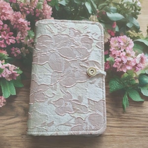May include: A pink floral patterned fabric notebook cover with a gold button closure.