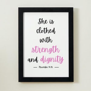May include: A black framed print with a white background and the text "She is clothed with strength and dignity - Proverbs 31:25 -" in black and pink lettering.