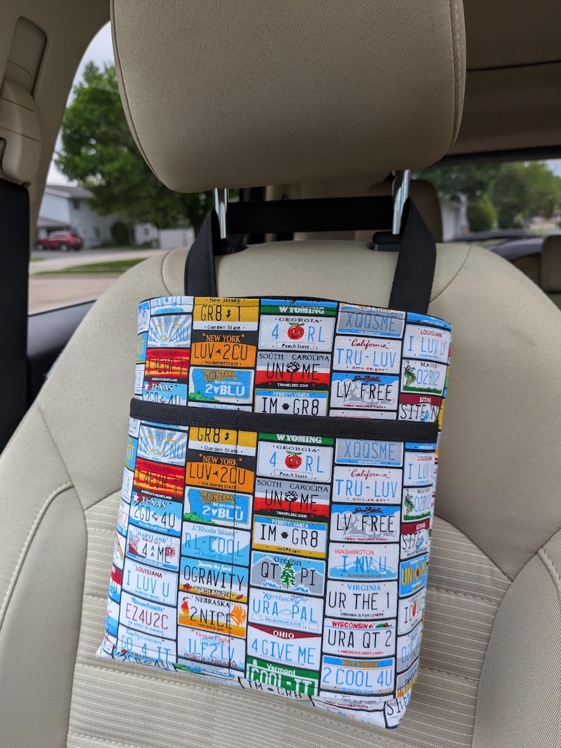 K&ouml;nnte beinhalten: Ein Autositz-Organizer mit einem farbenfrohen Nummernschildmuster. Der Organizer hat zwei schwarze Taschen und schwarze Tr&auml;ger zum Aufh&auml;ngen. Die Nummernschilder stammen aus verschiedenen Bundesstaaten, darunter New York, Wyoming und Louisiana.