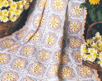 May include: A crocheted baby blanket with a daisy pattern in shades of white, blue, and peach. The blanket is folded and draped over a wooden surface.