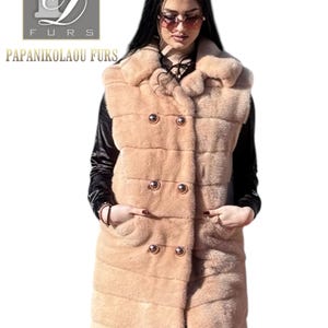 May include: A long, light brown fur vest with a double-breasted button closure and a large collar. The vest has two pockets and gold-toned buttons.