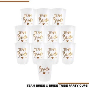 May include: A collection of clear plastic cups with gold lettering that reads "TEAM Bride" and "Bride". Each cup features a heart and arrow design. Ideal for a bridal party.