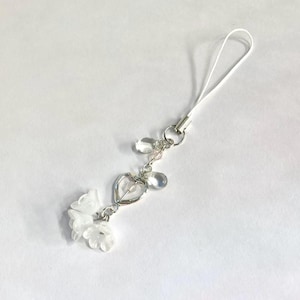May include: A white phone charm with a heart, clear beads, and flower-shaped charms.