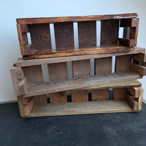 Pode incluir: Tr&ecirc;s caixas de madeira r&uacute;sticas empilhadas. As caixas retangulares apresentam ripas verticais e uma parte superior aberta. A madeira exibe tons de castanho vari&aacute;veis, sugerindo uma origem vintage ou reciclada. Ideais para armazenamento ou exibi&ccedil;&atilde;o.