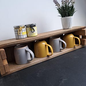 Pode incluir: Uma caneca de cer&acirc;mica branca com uma al&ccedil;a preta e o texto "But First, Coffee" em negrito preto. A caneca est&aacute; sobre um fundo desfocado, sugerindo um ambiente acolhedor.