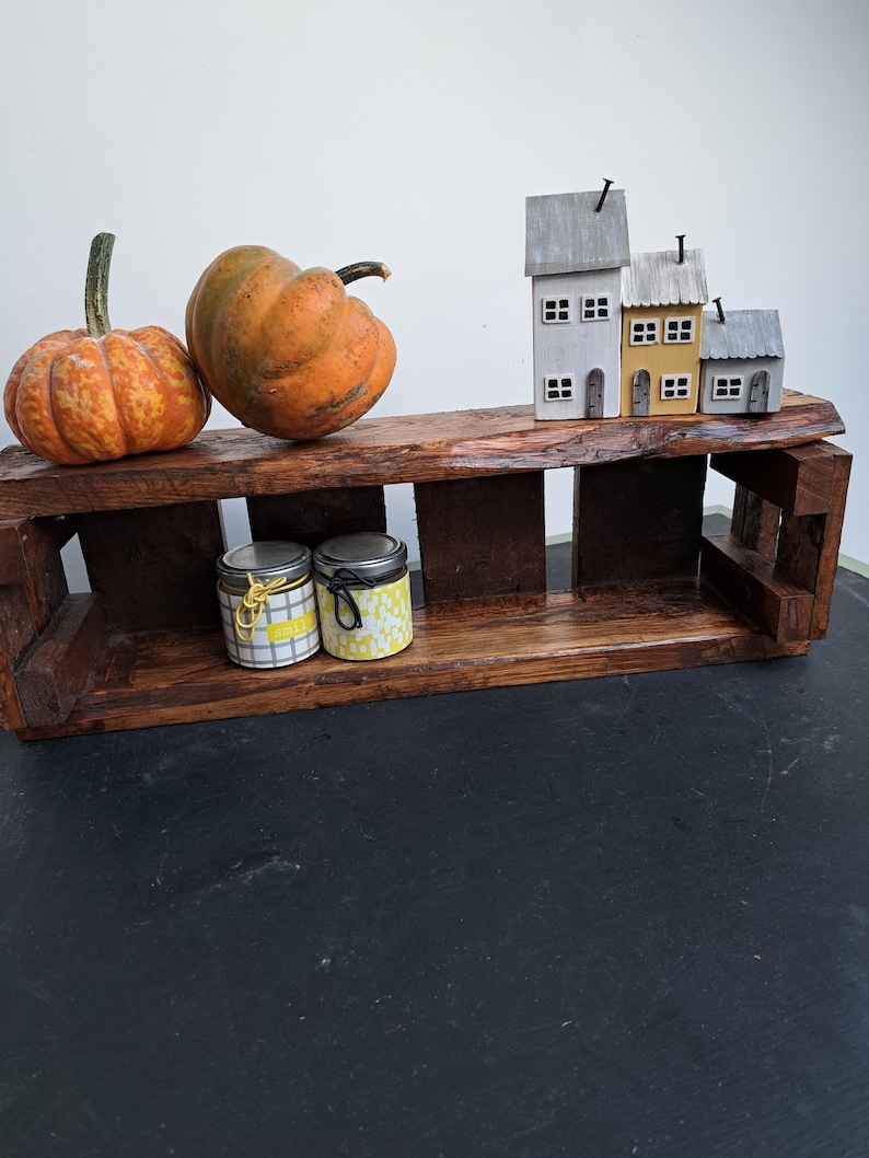Pode incluir: Uma prateleira r&uacute;stica de madeira escura exibe duas ab&oacute;boras laranja, tr&ecirc;s casas em miniatura e dois pequenos potes. A prateleira est&aacute; sobre uma superf&iacute;cie preta. Os potes t&ecirc;m tampas decorativas.
