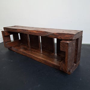 Pode incluir: Prateleira retangular de madeira castanha escura com borda natural na parte superior. A prateleira tem suportes verticais que criam compartimentos abertos. A madeira tem um tom rico e quente e gr&atilde;o vis&iacute;vel, sugerindo um design artesanal.