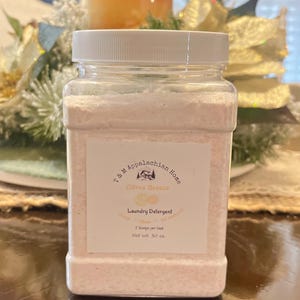 K&ouml;nnte beinhalten: Ein wei&szlig;er Plastikbeh&auml;lter gef&uuml;llt mit rosa Waschmittelpulver. Das Etikett lautet "T & M Appalachian Home Citrus Breeze Laundry Detergent 2 Scoops per load Net Wt. 30 oz."