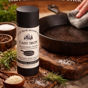 May include: A black and white cylindrical container of cast iron seasoning stick with the text "BEEF TALLOW" and "CAST IRON SEASONING STICK". The container is next to a cast iron skillet and wooden cutting boards.