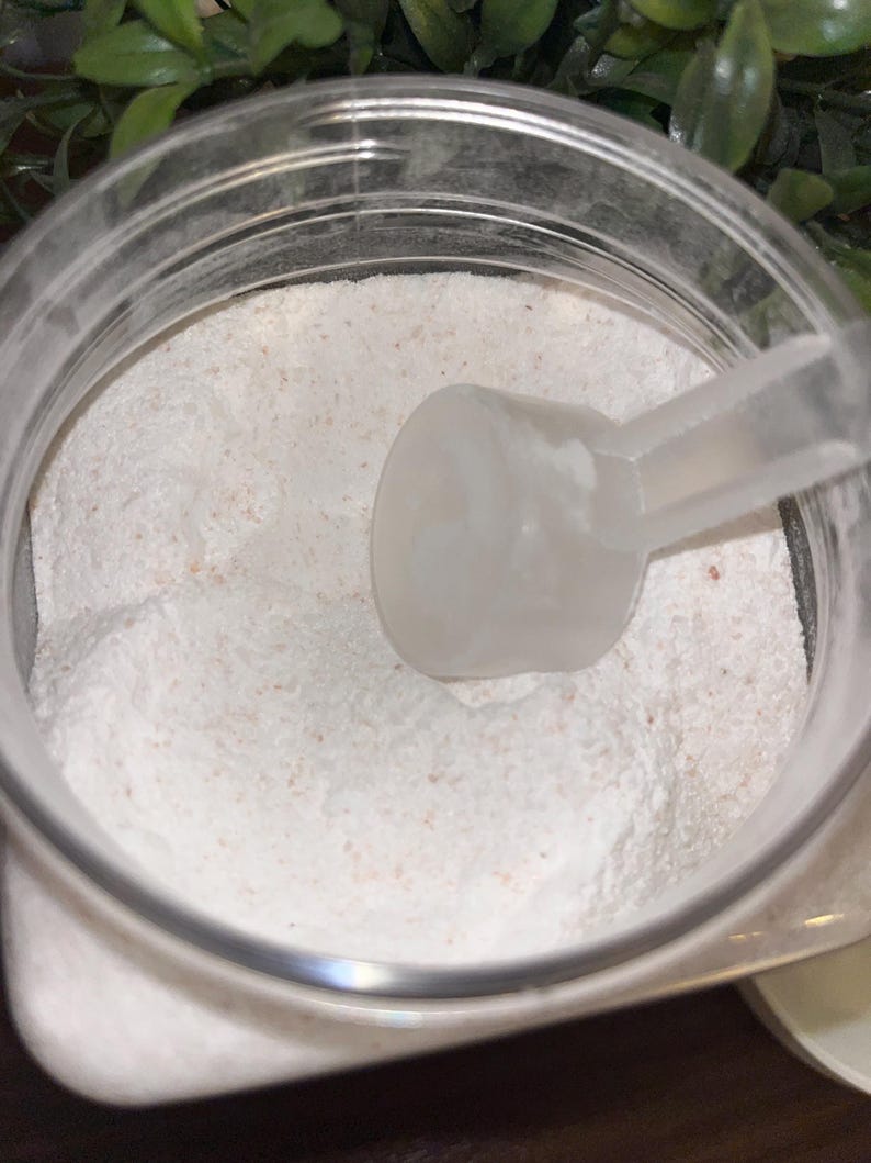 K&ouml;nnte beinhalten: Ein durchsichtiger Plastikbeh&auml;lter gef&uuml;llt mit wei&szlig;em Pulver und einer wei&szlig;en Plastikschaufel. Das Pulver hat einen leicht rosafarbenen Farbton.