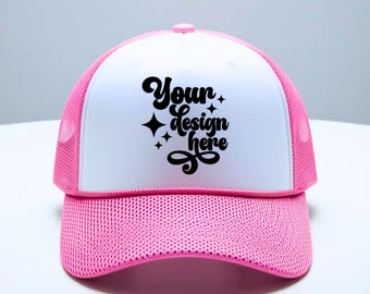 May include: A white and pink trucker hat with a black mesh back. The front of the hat has the text "Your design here" in a black cursive font with stars.