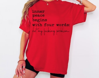 May include: A bright red t-shirt with the text "inner peace begins with four words: not my fucking problem" in black script. The shirt is a casual style, perfect for everyday wear.