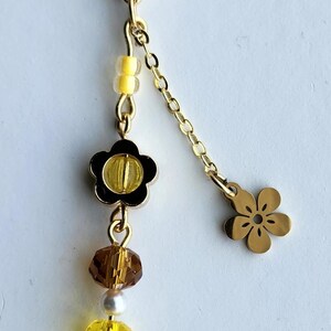 May include: A gold keychain with a flower charm, a small flower charm, and a variety of yellow and brown beads.