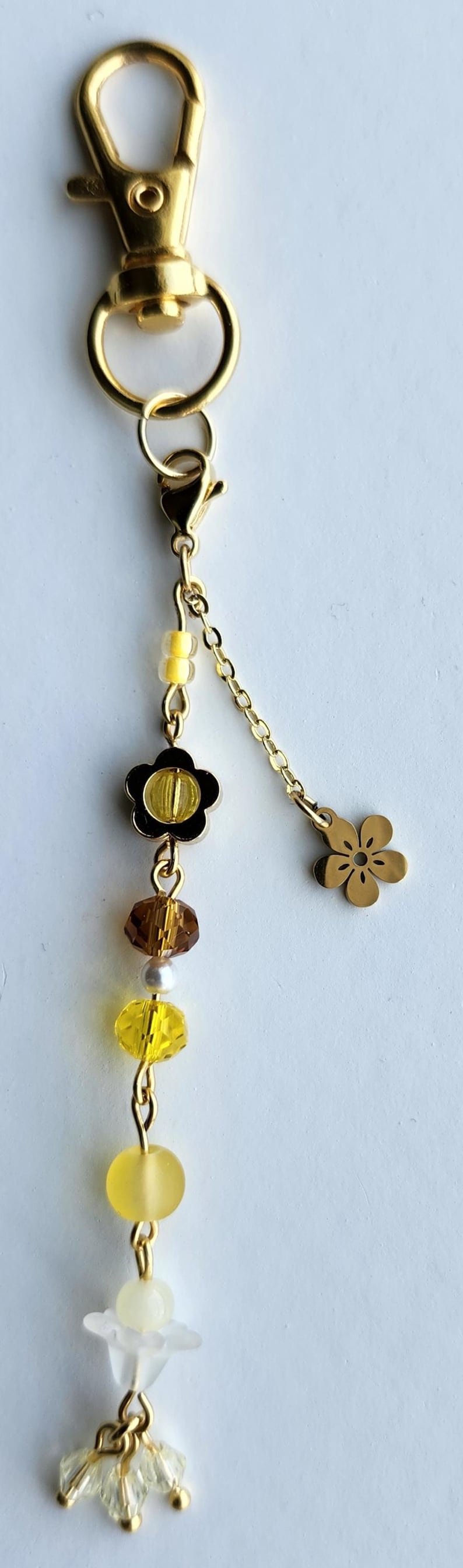 May include: A gold keychain with a flower charm, a small flower charm, and a variety of yellow and brown beads.