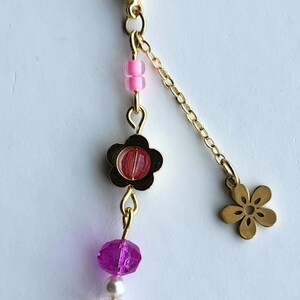 May include: A gold key chain with a pink and purple flower charm. The charm has a pink flower with a white center and a purple flower with a clear center. The key chain also has a small gold flower charm.