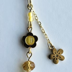 May include: A gold key chain with a yellow and gold flower charm, a yellow and gold bead, a clear bead, a yellow bead, and a gold flower charm with three yellow beads hanging from it.