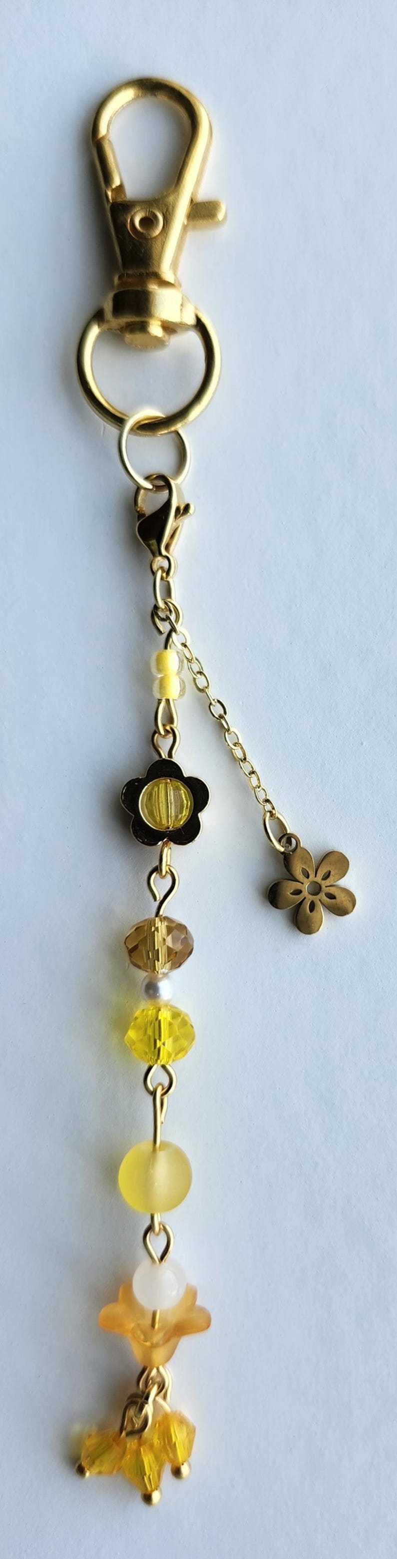 May include: A gold key chain with a yellow and gold flower charm, a yellow and gold bead, a clear bead, a yellow bead, and a gold flower charm with three yellow beads hanging from it.