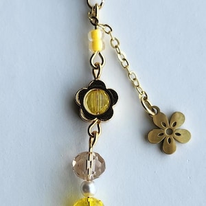 May include: A gold keychain with a yellow flower charm, yellow and clear glass beads, and a small gold flower charm. The keychain is attached to a gold split ring.
