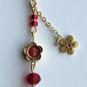 May include: A gold key chain with a red and pink beaded charm. The charm features a red flower with a pink center, red and pink beads, and a gold flower charm.