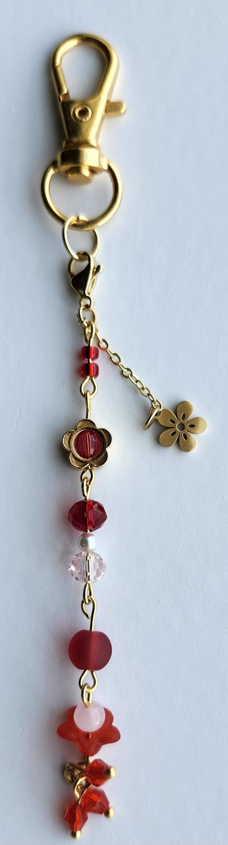 May include: A gold key chain with a red and pink beaded charm. The charm features a red flower with a pink center, red and pink beads, and a gold flower charm.