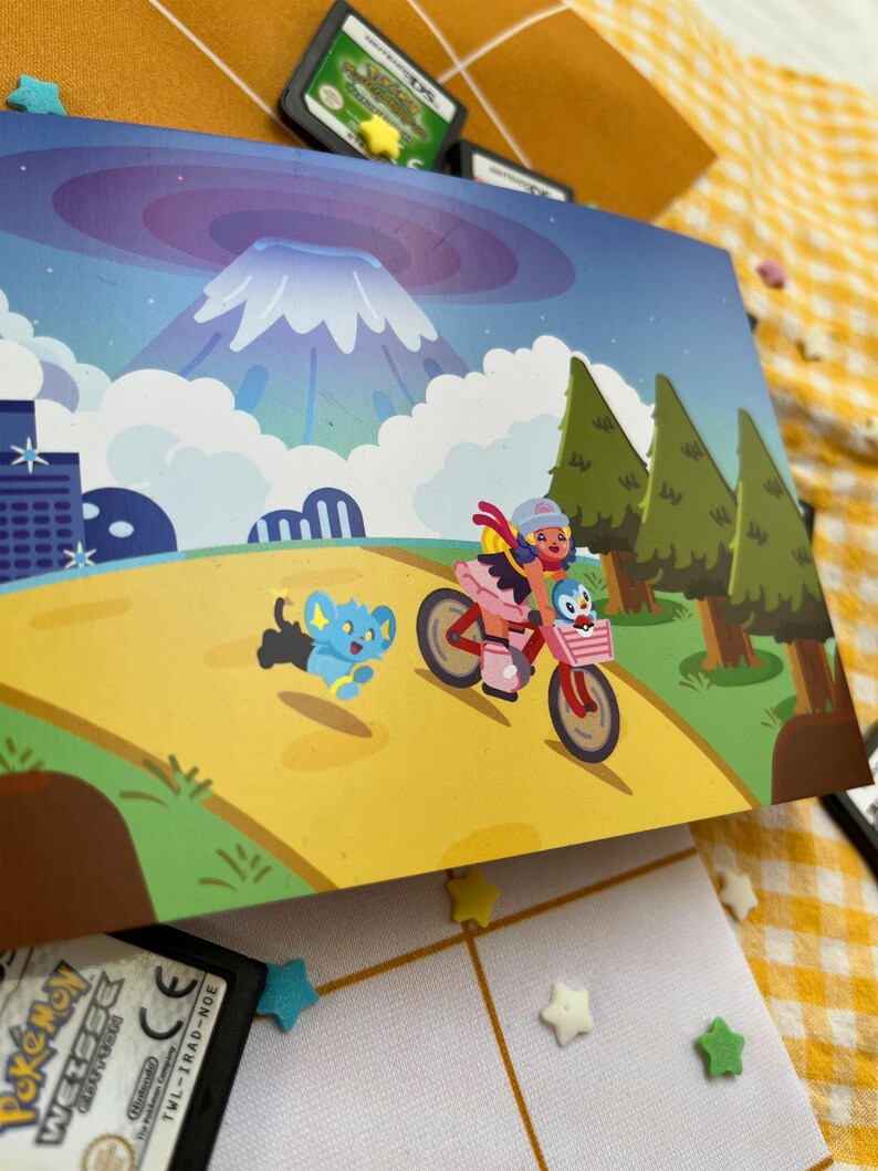 Może przedstawiać: Kolorowa ilustracja przedstawia osobę na r&oacute;żowym rowerze z koszykiem, w towarzystwie niebieskiego stworzenia. Tło przedstawia g&oacute;rę, drzewa i panoramę miasta. Widoczne są r&oacute;wnież kartridże do gier i dekoracje w kształcie gwiazd.