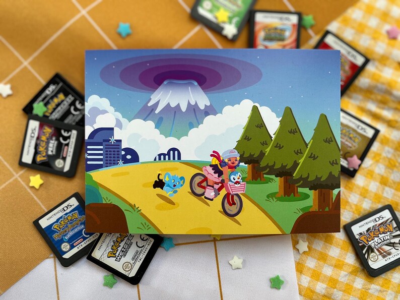 Może przedstawiać: Kolorowa ilustracja przedstawia osobę jadącą na r&oacute;żowym rowerze z koszykiem, w towarzystwie postaci z kresk&oacute;wek. W tle g&oacute;ra, drzewa i krajobraz miejski. Obraz otaczają liczne kartridże do gier Pokemon DS.