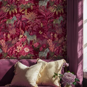 Pode incluir: Uma cena interior vibrante com um sofá magenta com almofadas creme com franjas. O fundo é um papel de parede rico com zebras, flores e folhagem tropical. Um vaso de flores cor-de-rosa está numa mesa lateral.