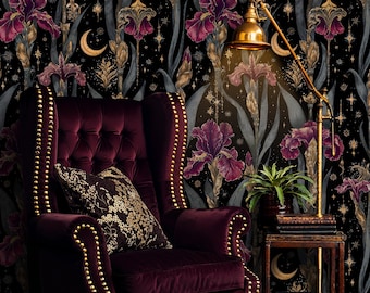May include: A deep burgundy velvet armchair with gold studding and a patterned cushion is set against black floral wallpaper. A gold lamp and small side table with books complete the scene. The wallpaper features irises, moons, and stars.