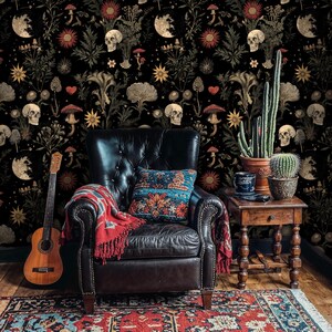 May include: A black leather armchair with a red throw blanket and a blue and white patterned pillow sits in front of a wall covered in dark floral wallpaper with skulls and other botanical motifs.